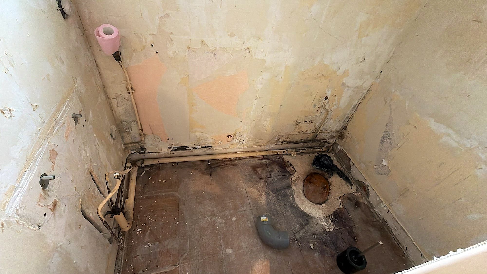 Toilettes à Lille avant travaux, murs dégradés, anciens papiers peints arrachés et tuyauterie apparente