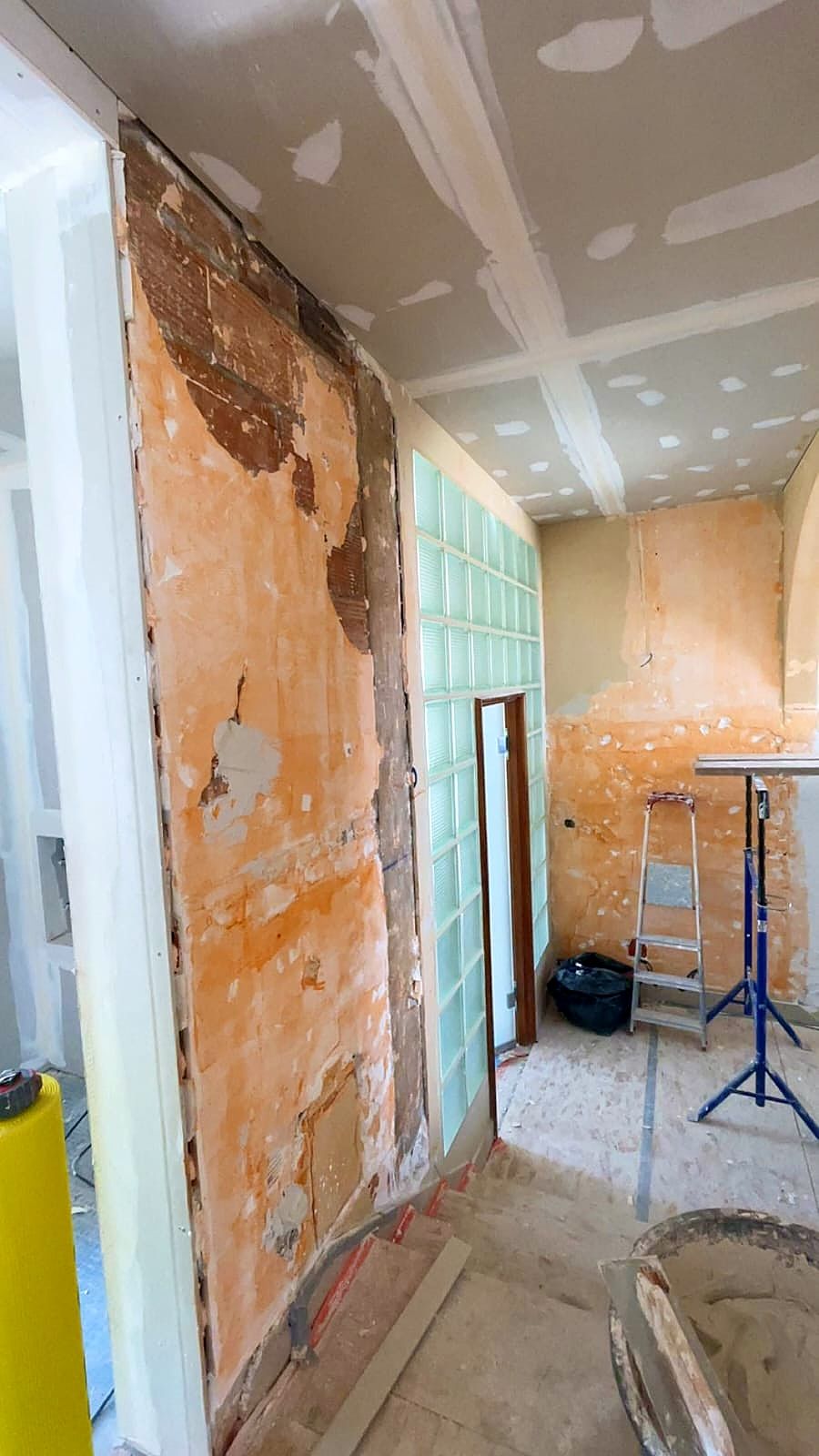 Couloir à Dunkerque avant travaux, mur décroûté avec restes d’anciens revêtements, près d’une cloison en pavés de verre